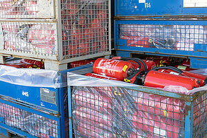 Ausgemusterte Feuerlöscher liegen in Gitterboxen, um recycelt zu werden